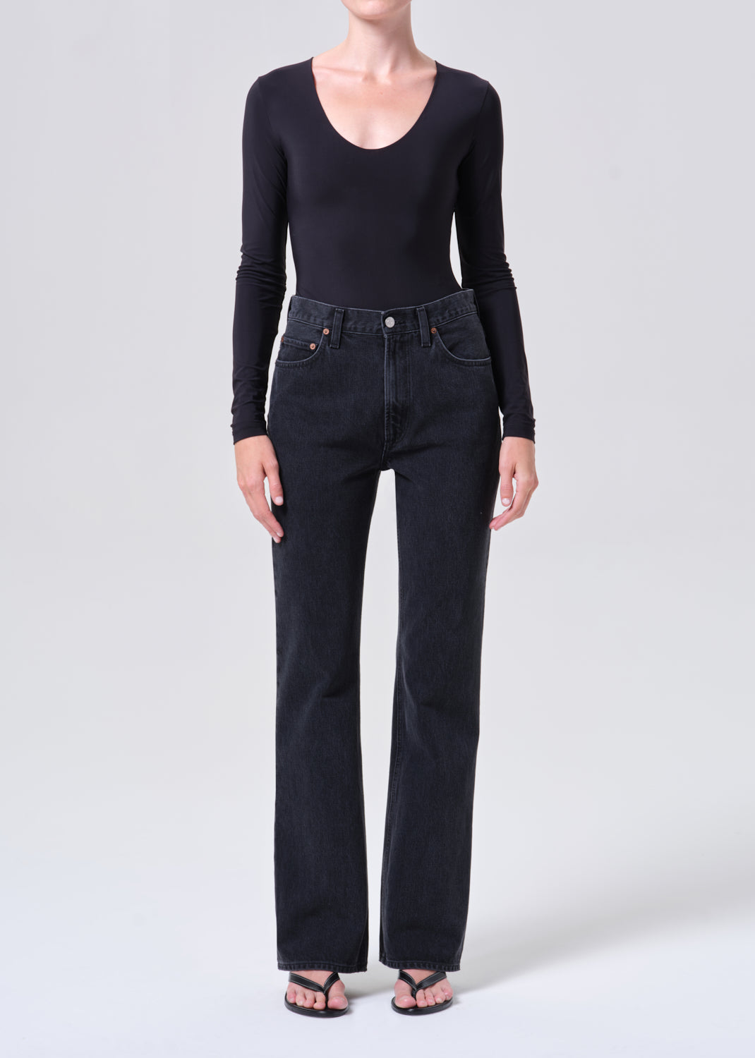 Person wearing a black long-sleeve top and dark jeans on a white background