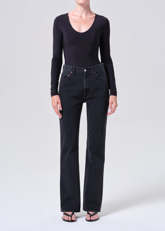 Person wearing a black long-sleeve top and dark jeans on a white background