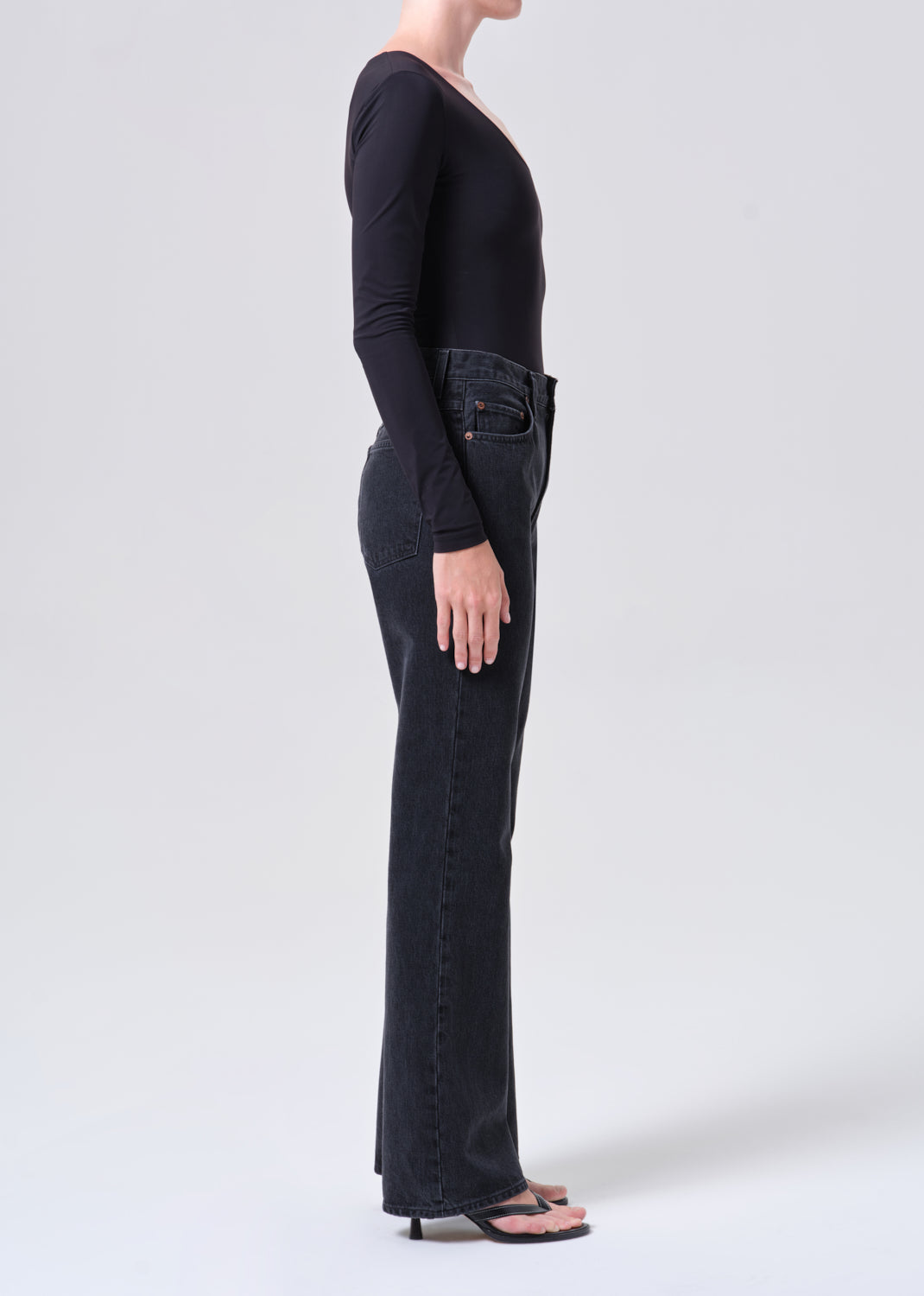 Person wearing black long-sleeve top and dark jeans on a white background