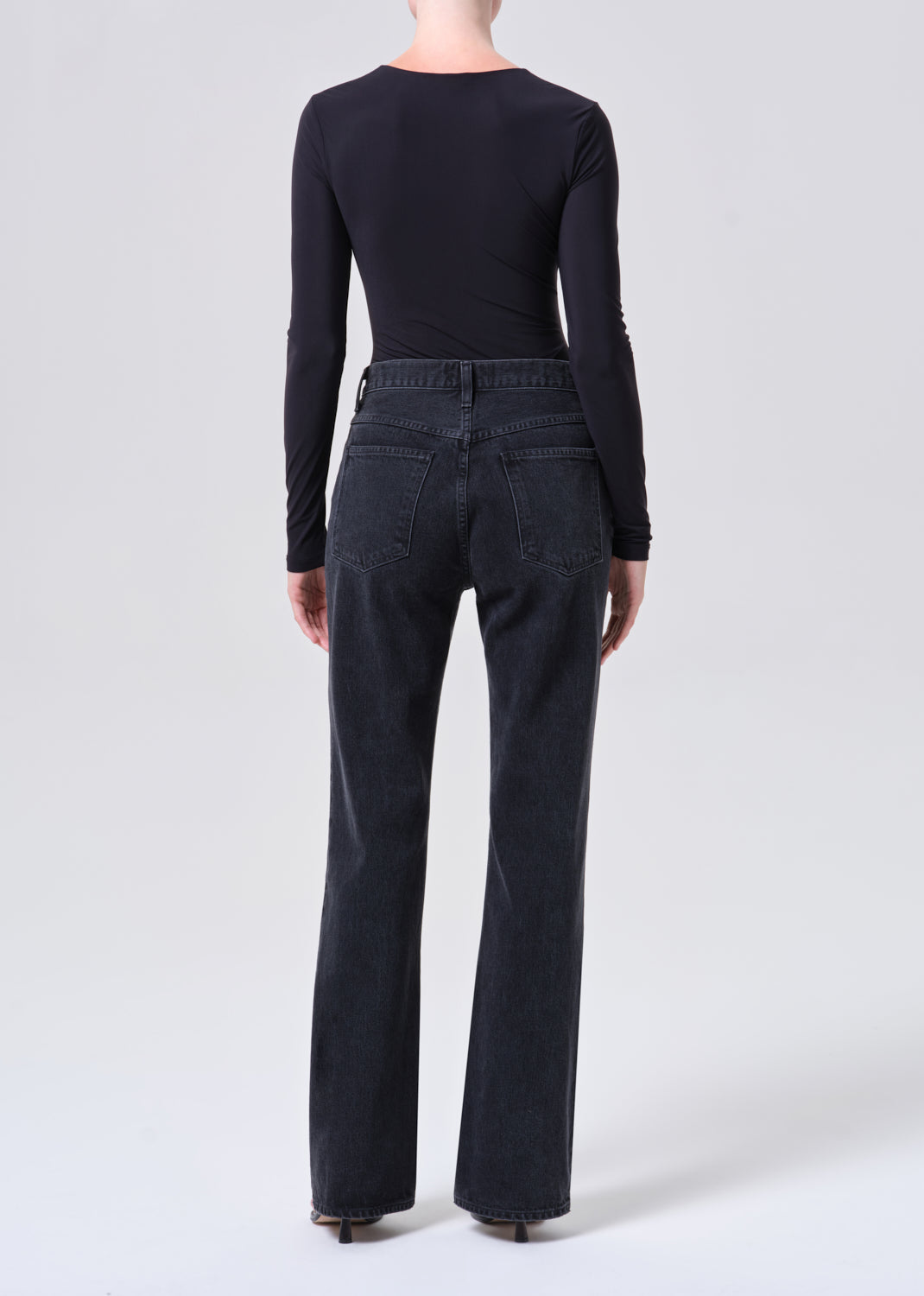 Person wearing black long-sleeve top and dark jeans on a white background