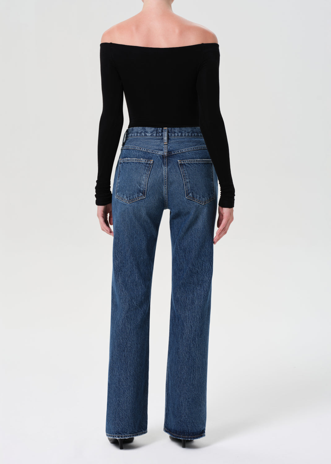 Person wearing blue jeans and a black off-shoulder top on a white background