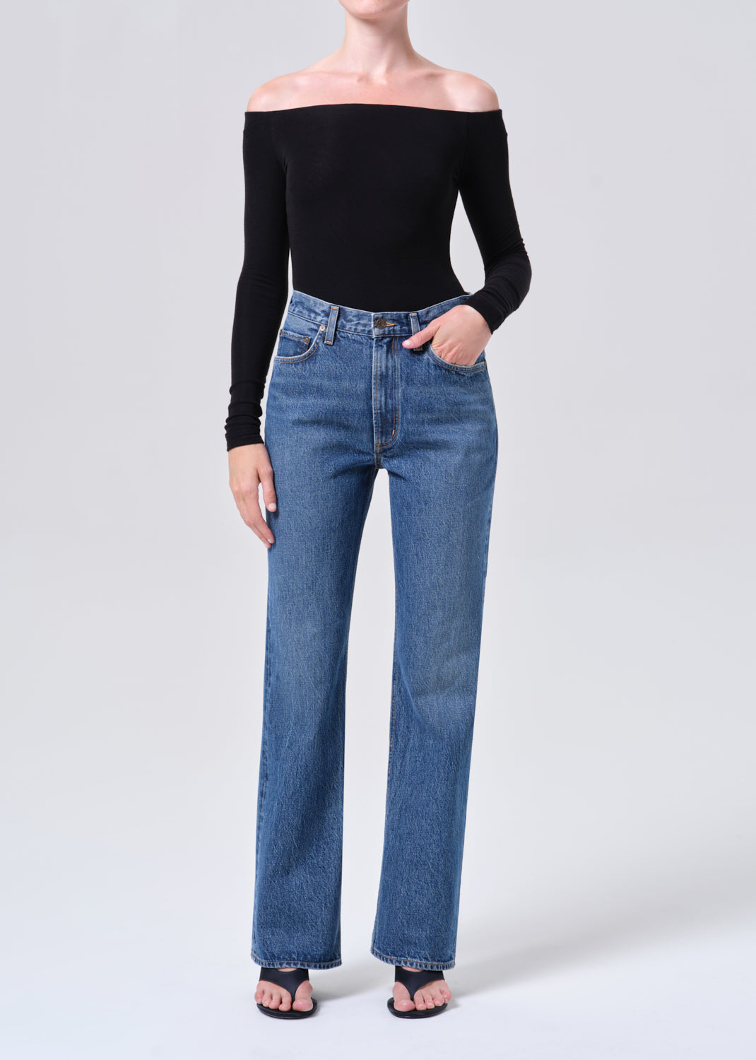 Person wearing a black off-shoulder top and blue jeans on a white background