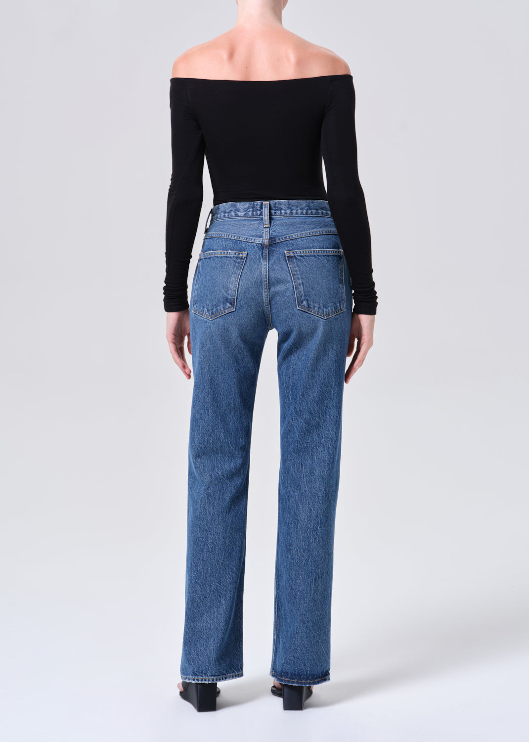 Person wearing blue jeans and a black off-shoulder top on a white background