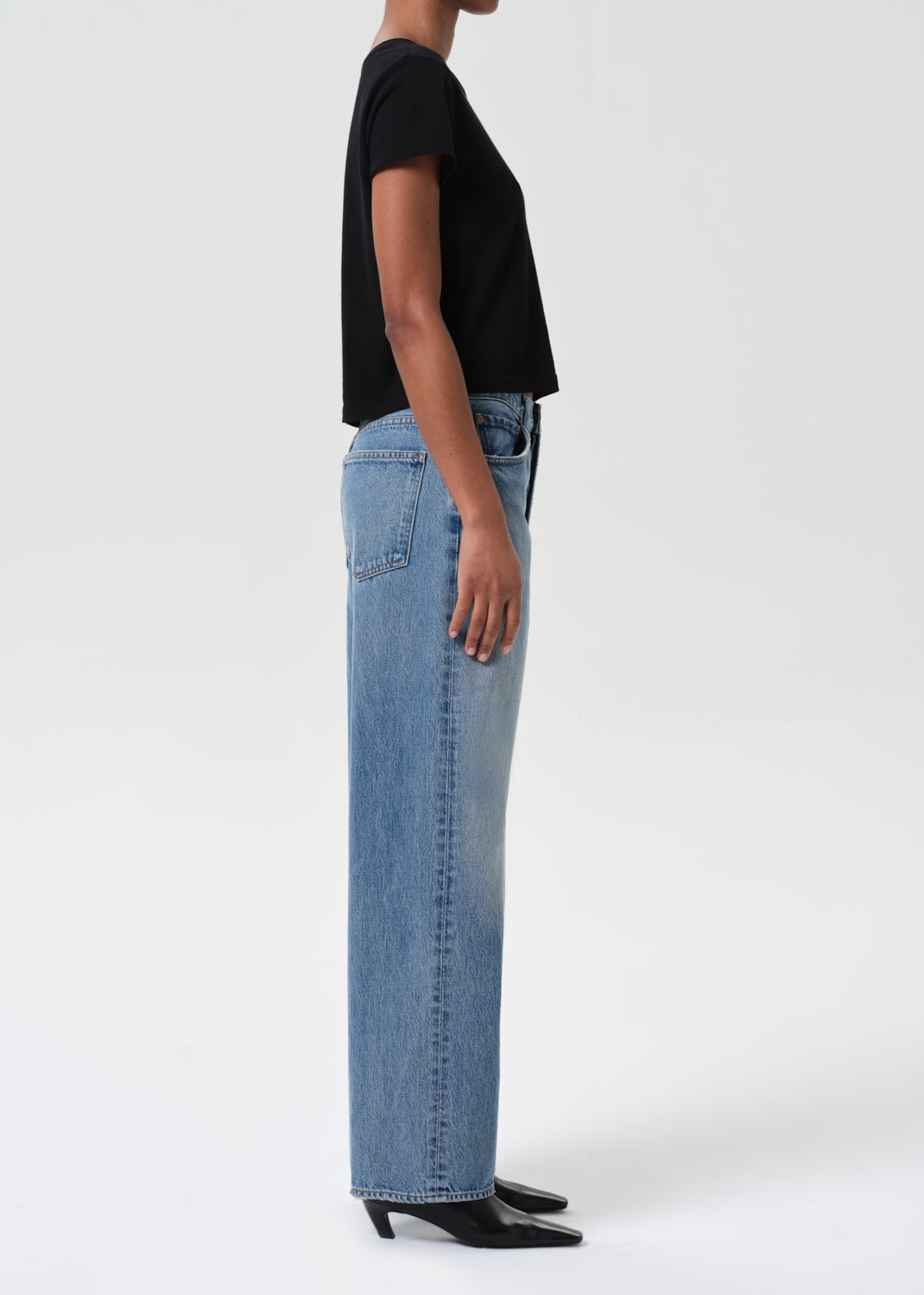 Person wearing blue jeans and a black top on a white background