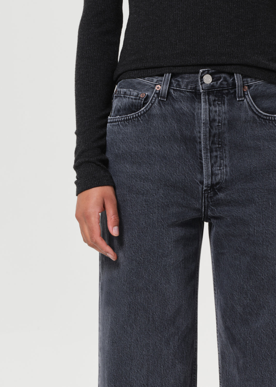 Person wearing dark blue jeans and a black long-sleeve shirt on a light gray background