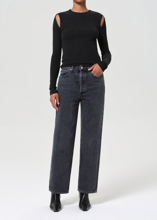 Person wearing a black long-sleeve top with cut-out design and dark jeans on a white background