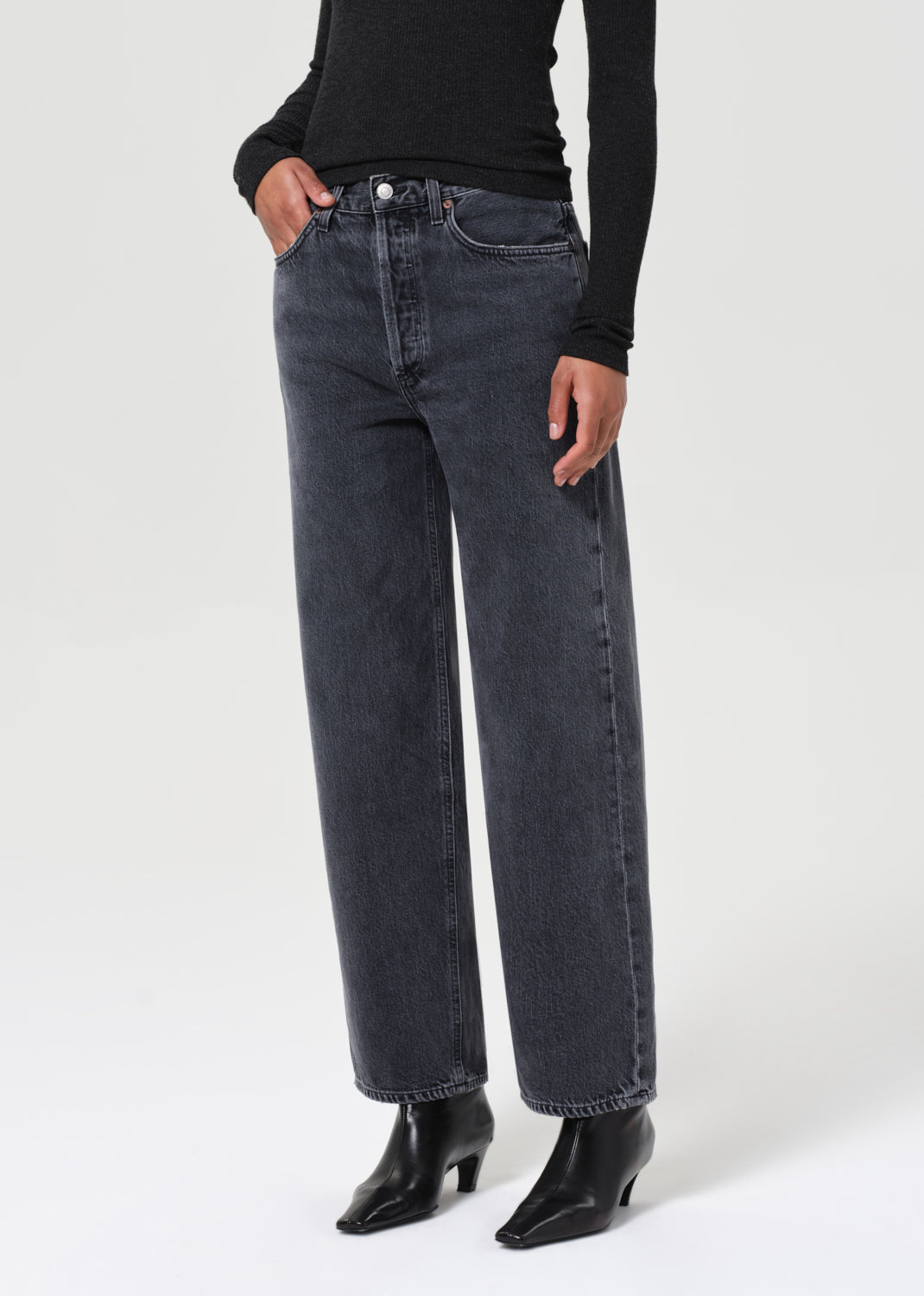 Person wearing dark blue jeans and black shoes on a white background