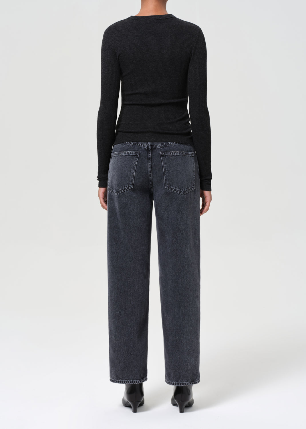Person wearing black long-sleeve top and dark gray jeans on a white background