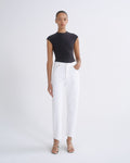 A model stands against a plain white studio background wearing a black sleeveless mock-neck top, white wide-leg cropped jeans, and beige strappy sandals.