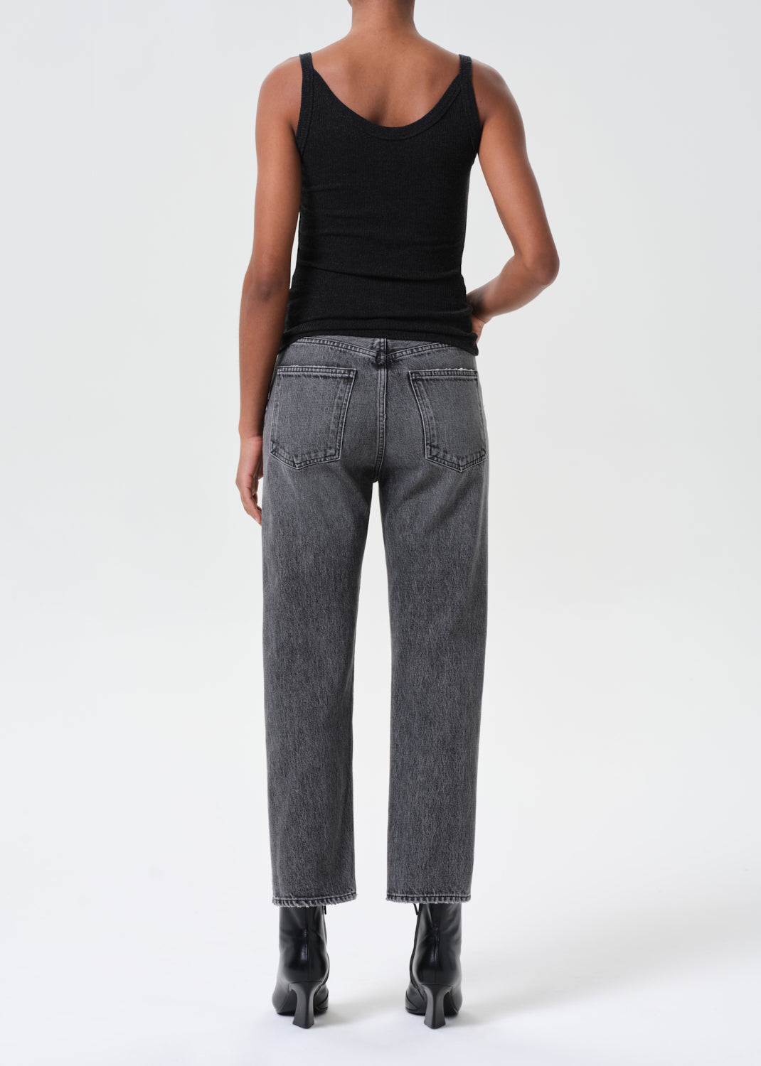 Person wearing black tank top and gray jeans on a white background