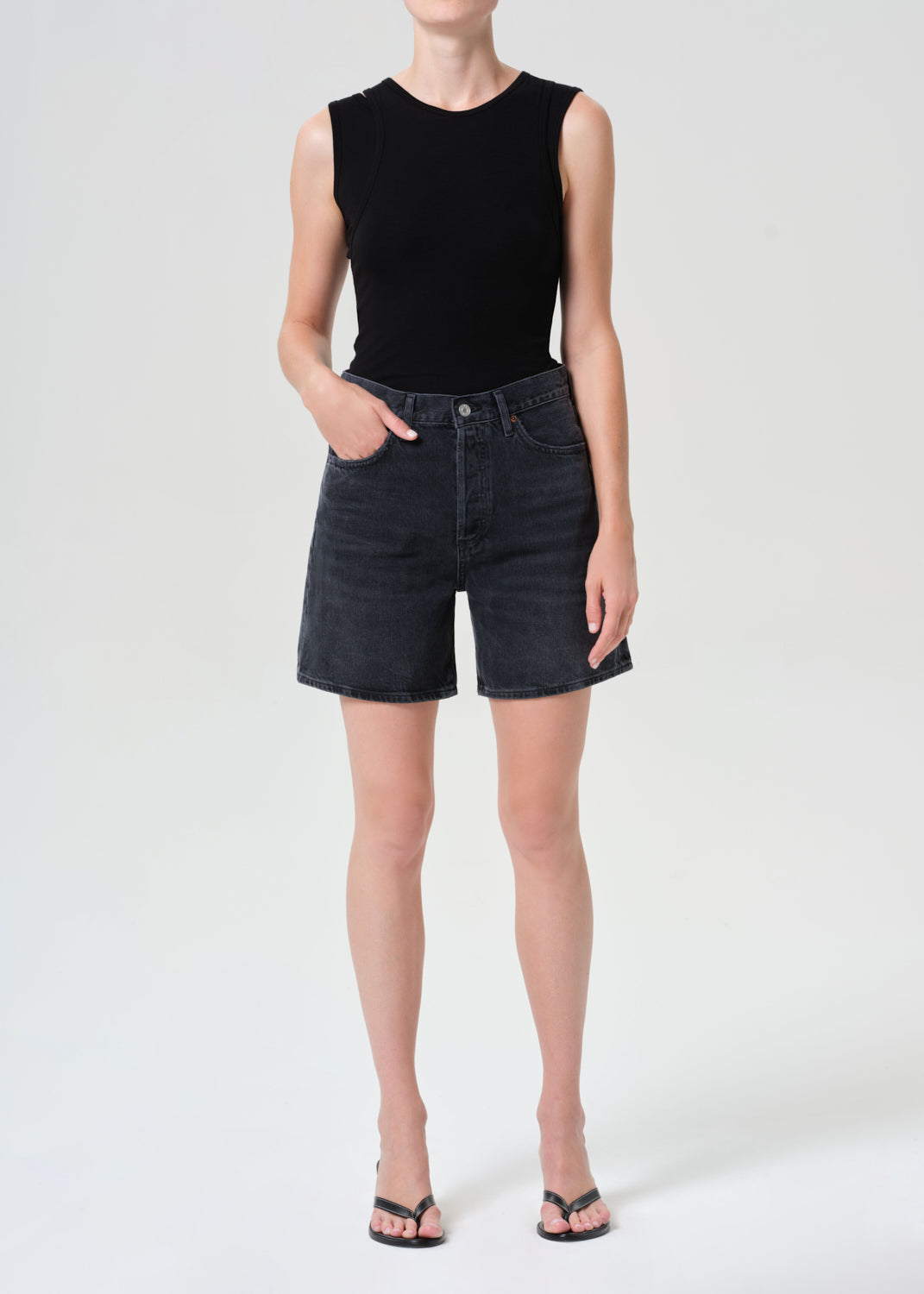 Person wearing a black sleeveless top and dark denim shorts on a white background