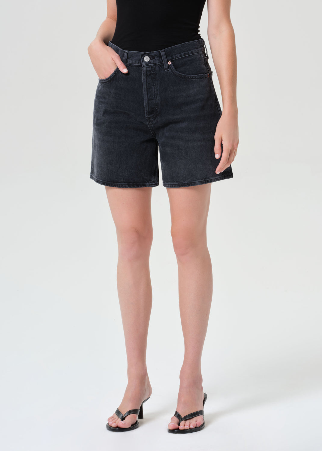 Person wearing black denim shorts on a white background