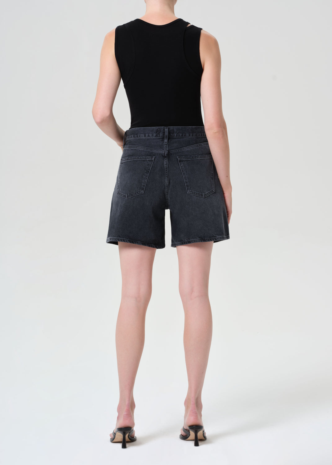 Person wearing a black sleeveless top and dark denim shorts on a white background