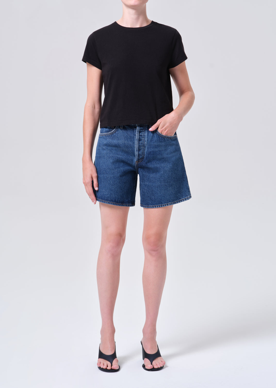 Person wearing a black t-shirt and blue denim shorts on a white background