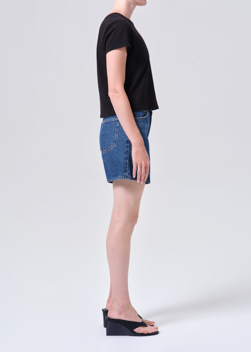 Person wearing a black t-shirt and blue denim shorts on a white background