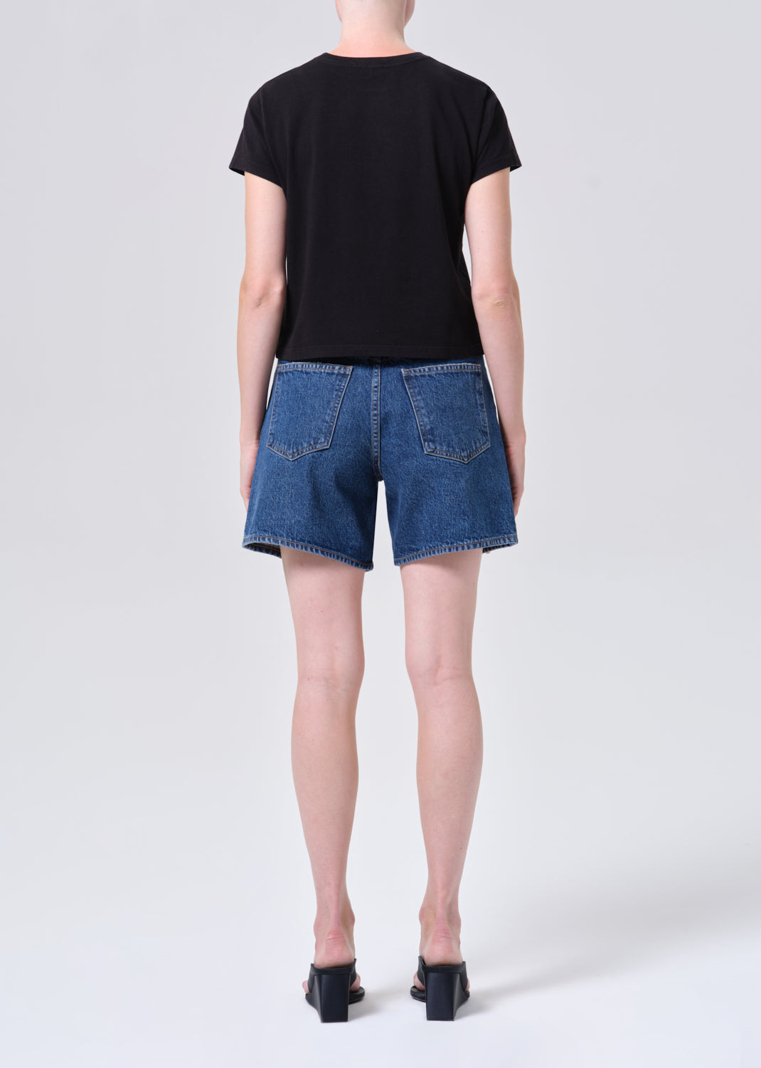 Person wearing a black t-shirt and blue denim shorts on a white background