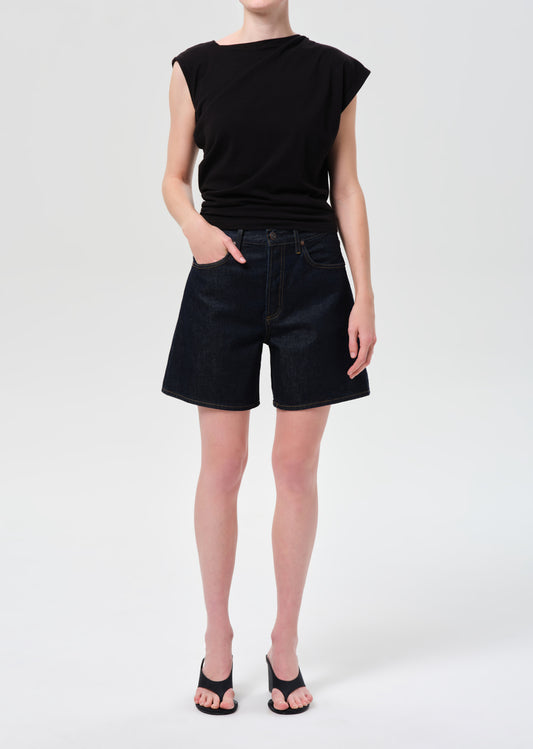 Person wearing a black sleeveless top and black denim shorts on a white background