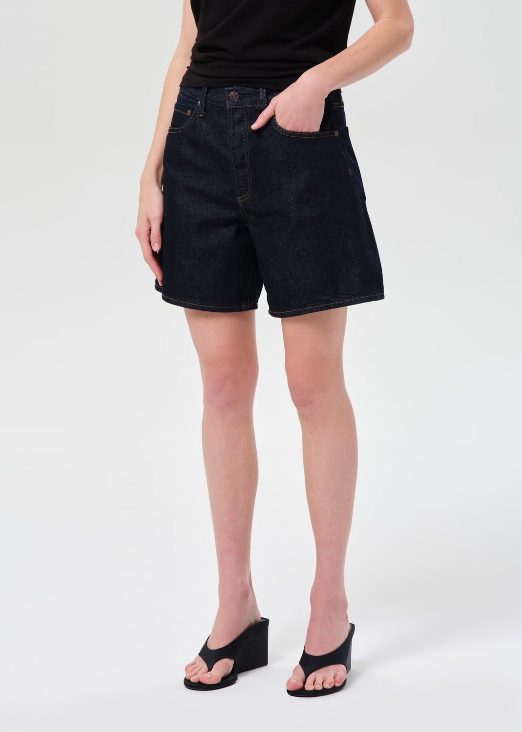 Person wearing black denim shorts on a white background
