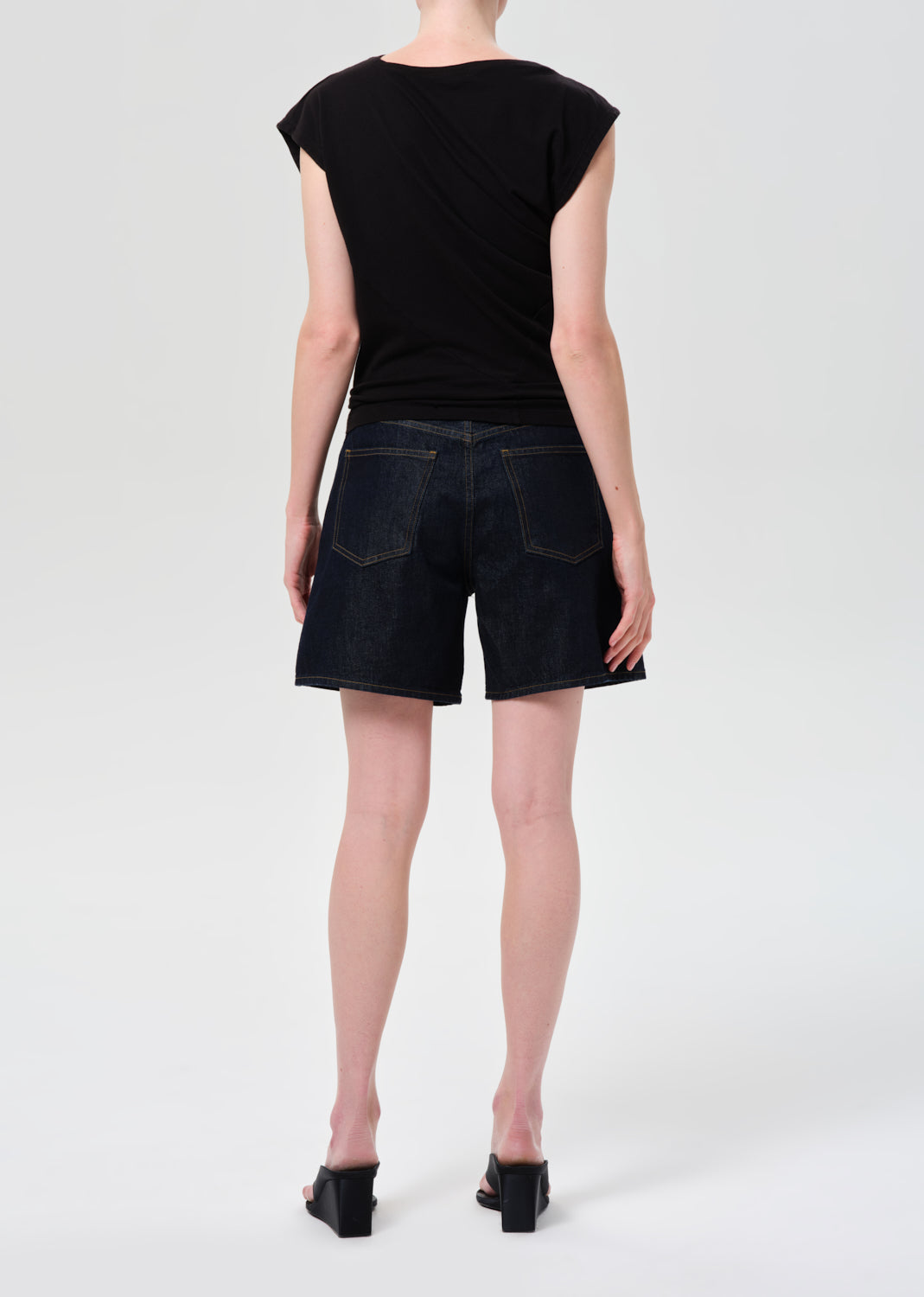 Person wearing a black top and black denim shorts on a white background