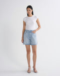 A woman modeling a white short-sleeve crewneck t-shirt and light-wash denim shorts against a plain light gray studio background.