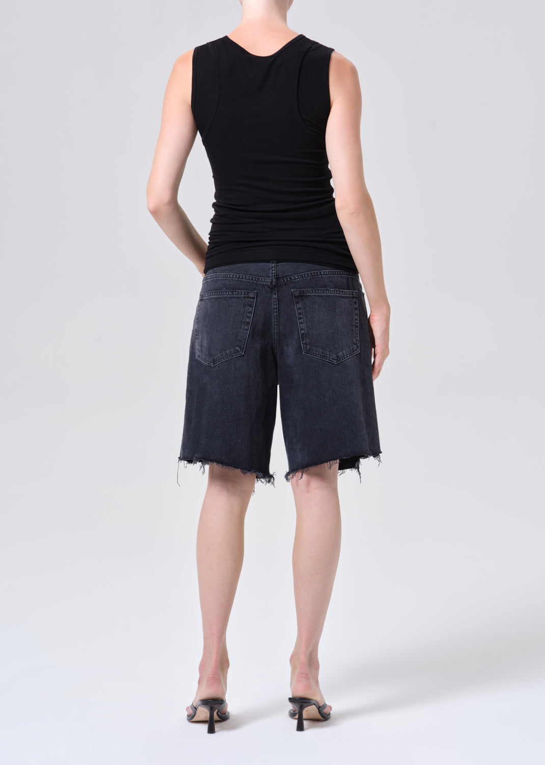 Person wearing black sleeveless top and denim shorts on a white background