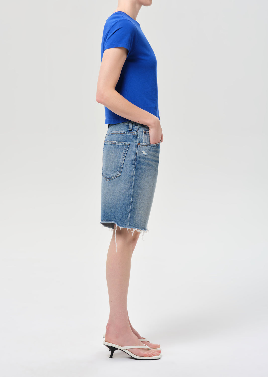 Person wearing a blue t-shirt and denim skirt on a white background