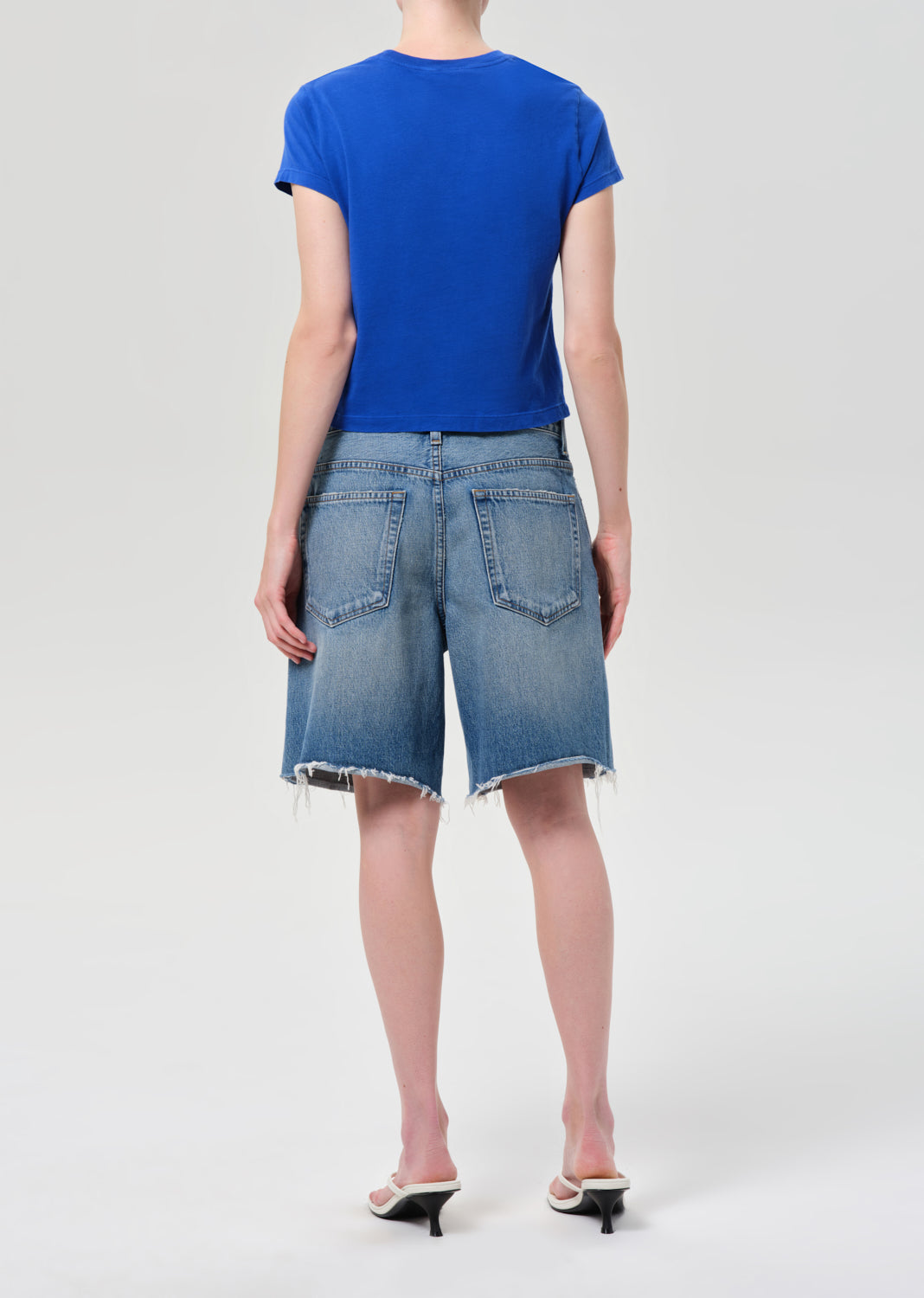 Person wearing a blue top and denim shorts on a white background