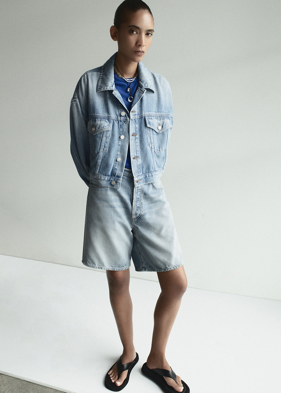 Person wearing a light blue denim jacket and shorts on a white background