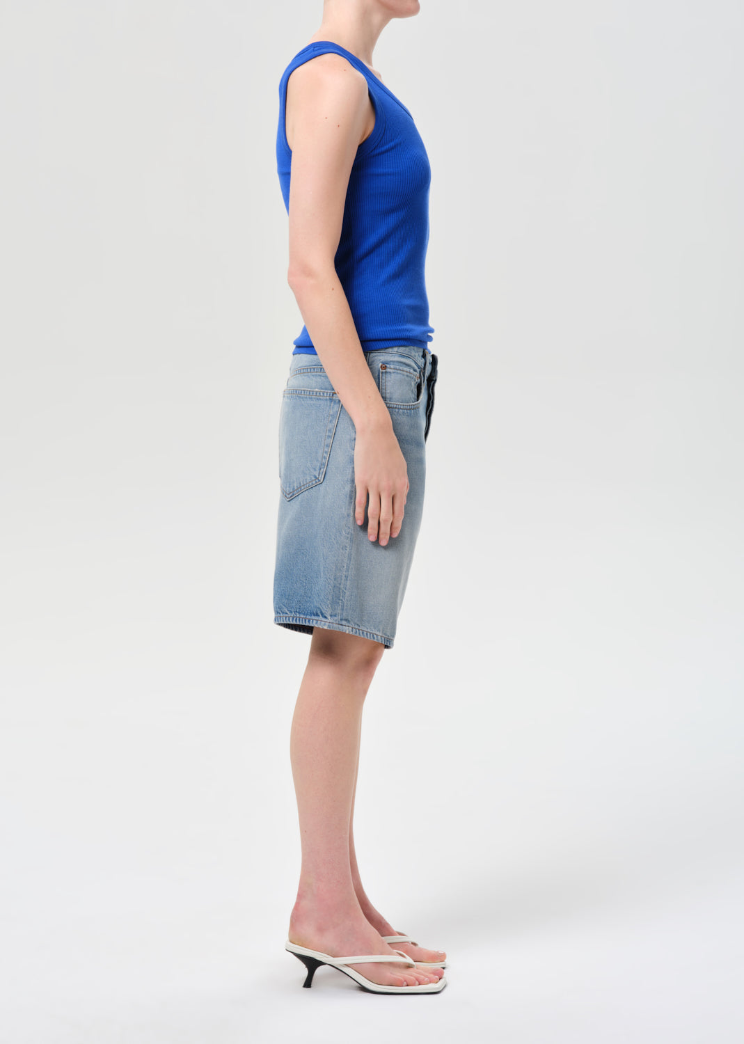 Person wearing a blue sleeveless top and denim skirt on a white background