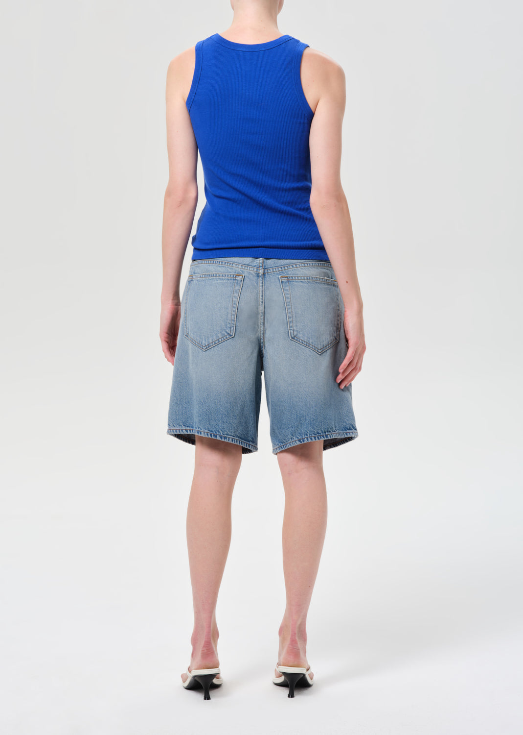Person wearing a blue sleeveless top and denim shorts on a white background