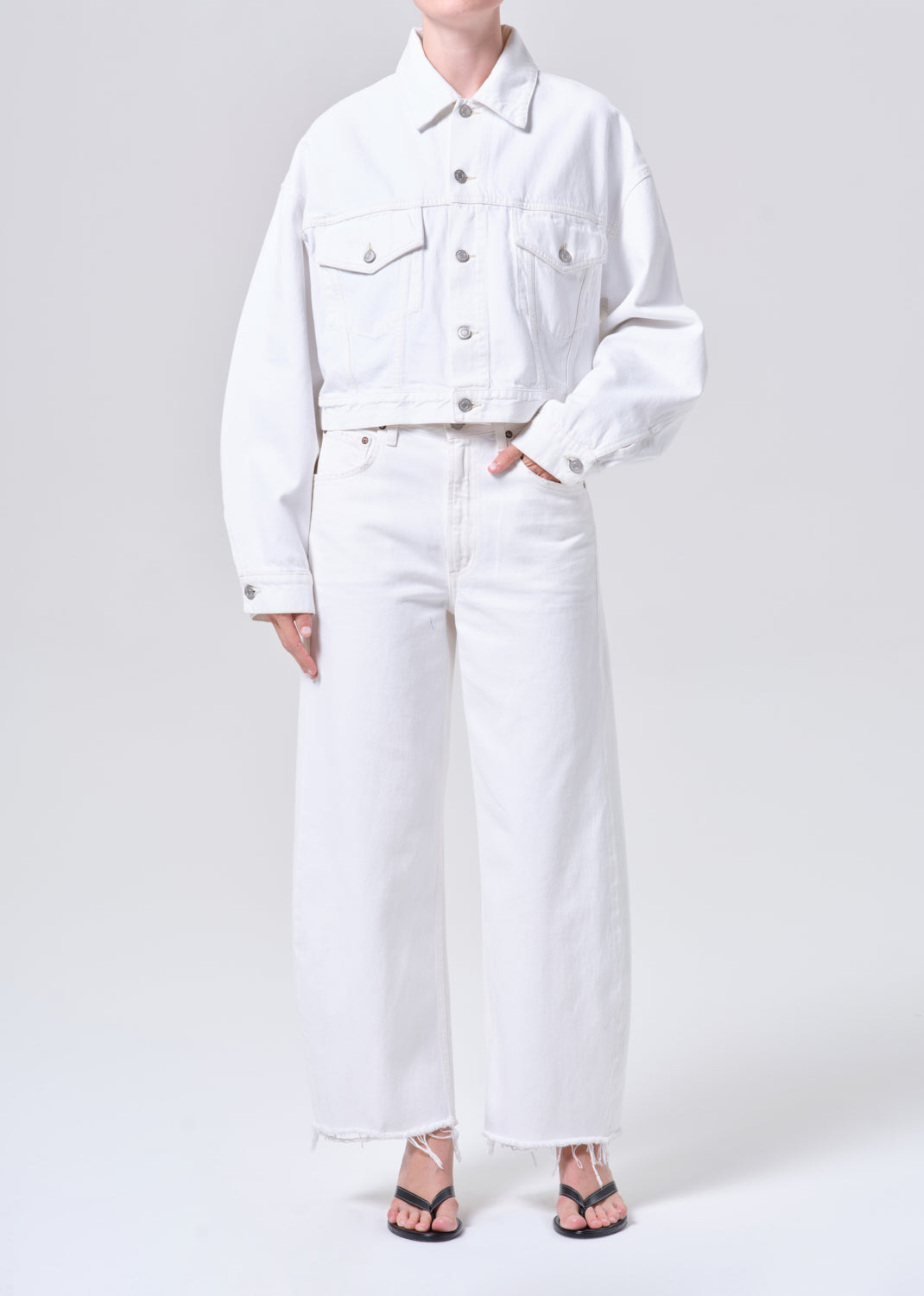 Person wearing a white denim jacket and pants on a plain background