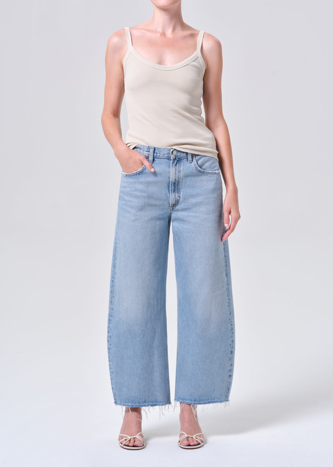Person wearing light blue jeans and a beige tank top on a white background