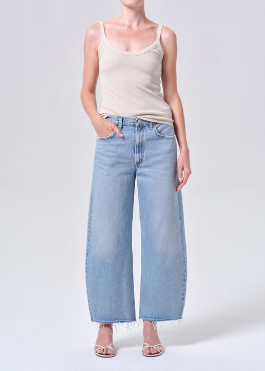Person wearing light blue jeans and a beige tank top on a white background