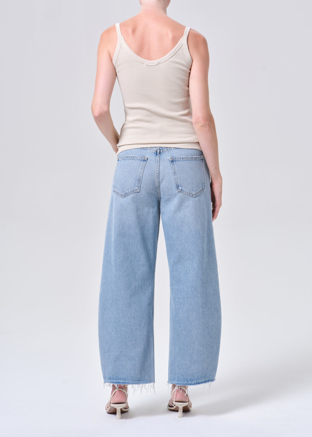 Person wearing a beige tank top and light blue jeans on a white background