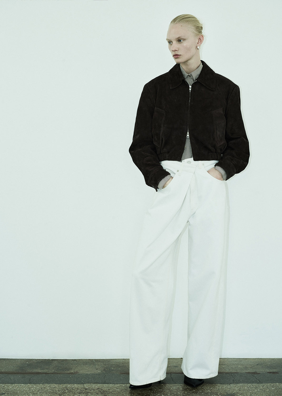 Person wearing a black jacket and white pants against a plain background
