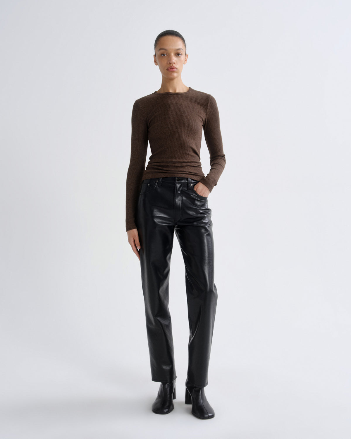 Person wearing a brown long-sleeve top and black leather pants on a white background