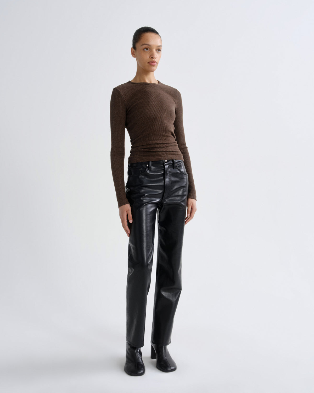Person wearing a brown long-sleeve top and black leather pants on a white background