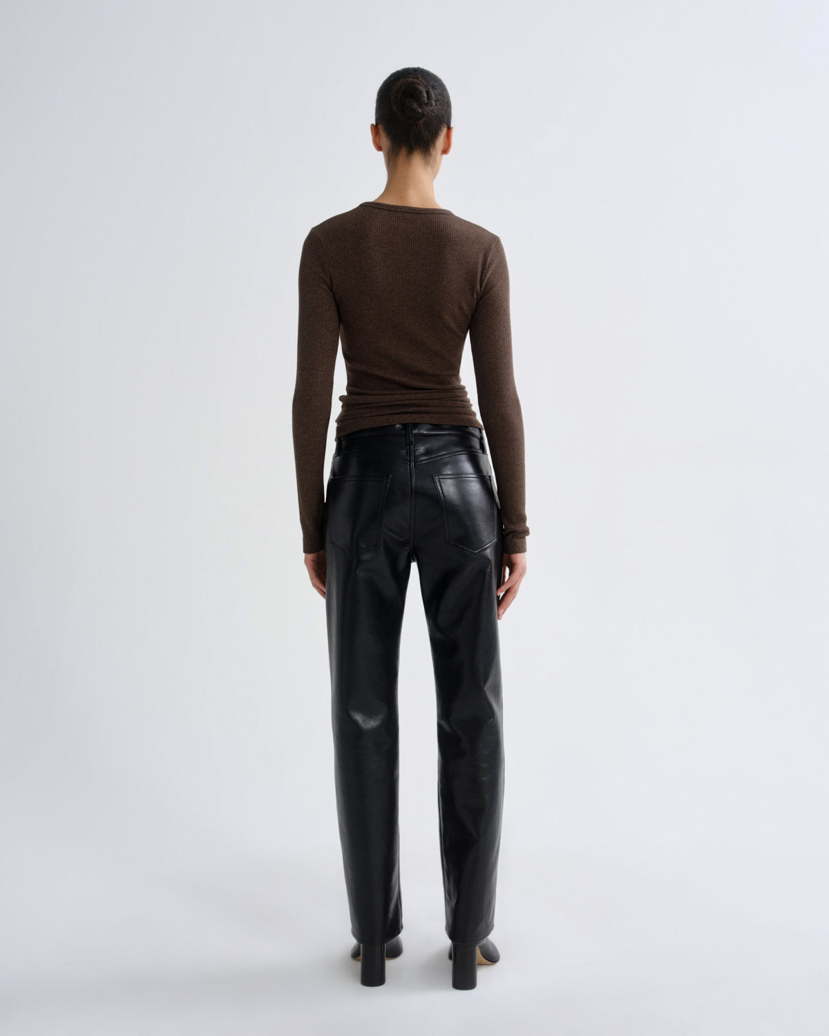 Person wearing a brown long-sleeve top and black leather pants on a white background