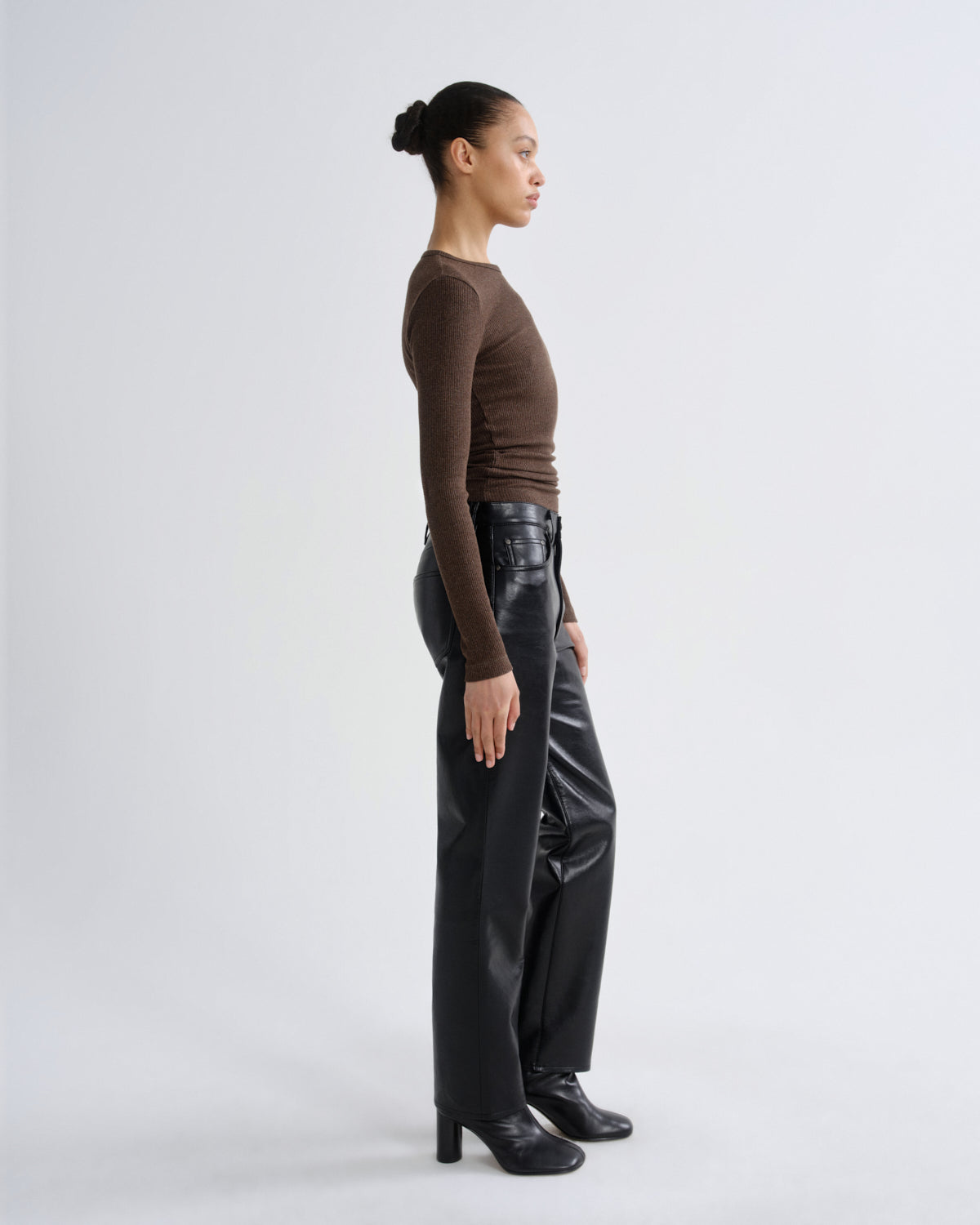 Person wearing a brown long-sleeve top and black leather pants on a white background