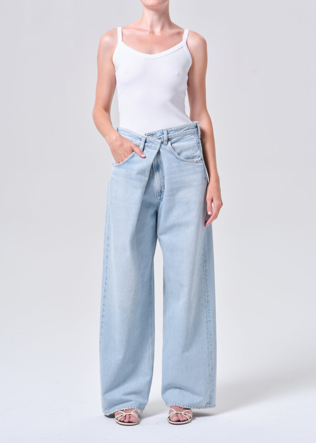 Person wearing light blue jeans and a white tank top on a plain background