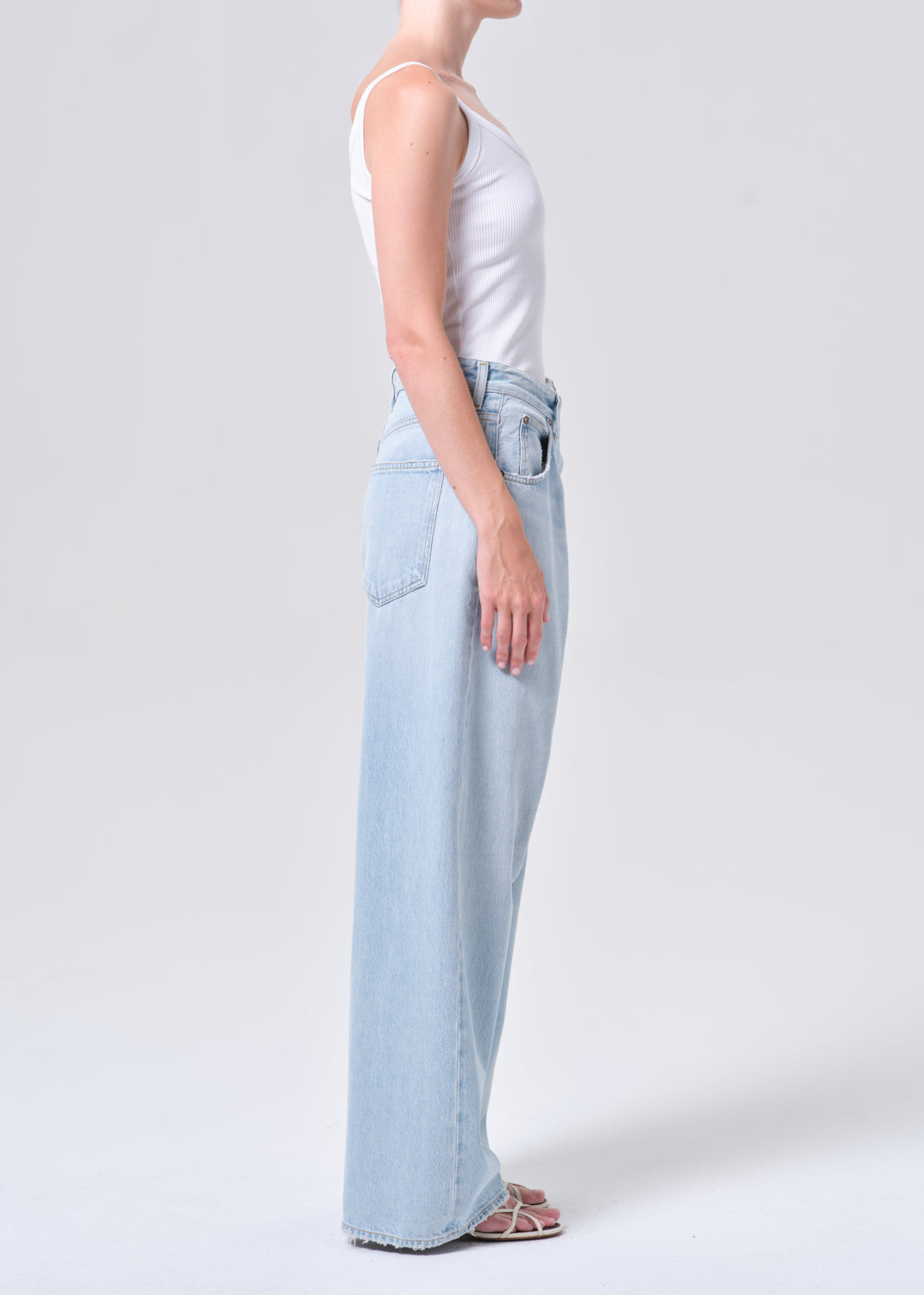 Person wearing light blue jeans and a white top on a plain background