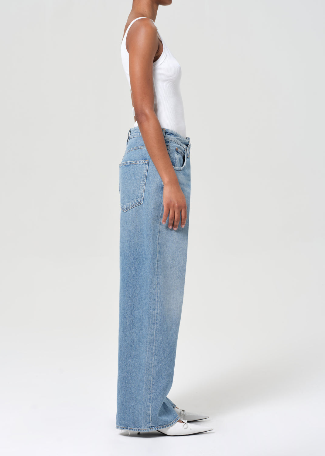 Person wearing light blue jeans and a white top on a plain background