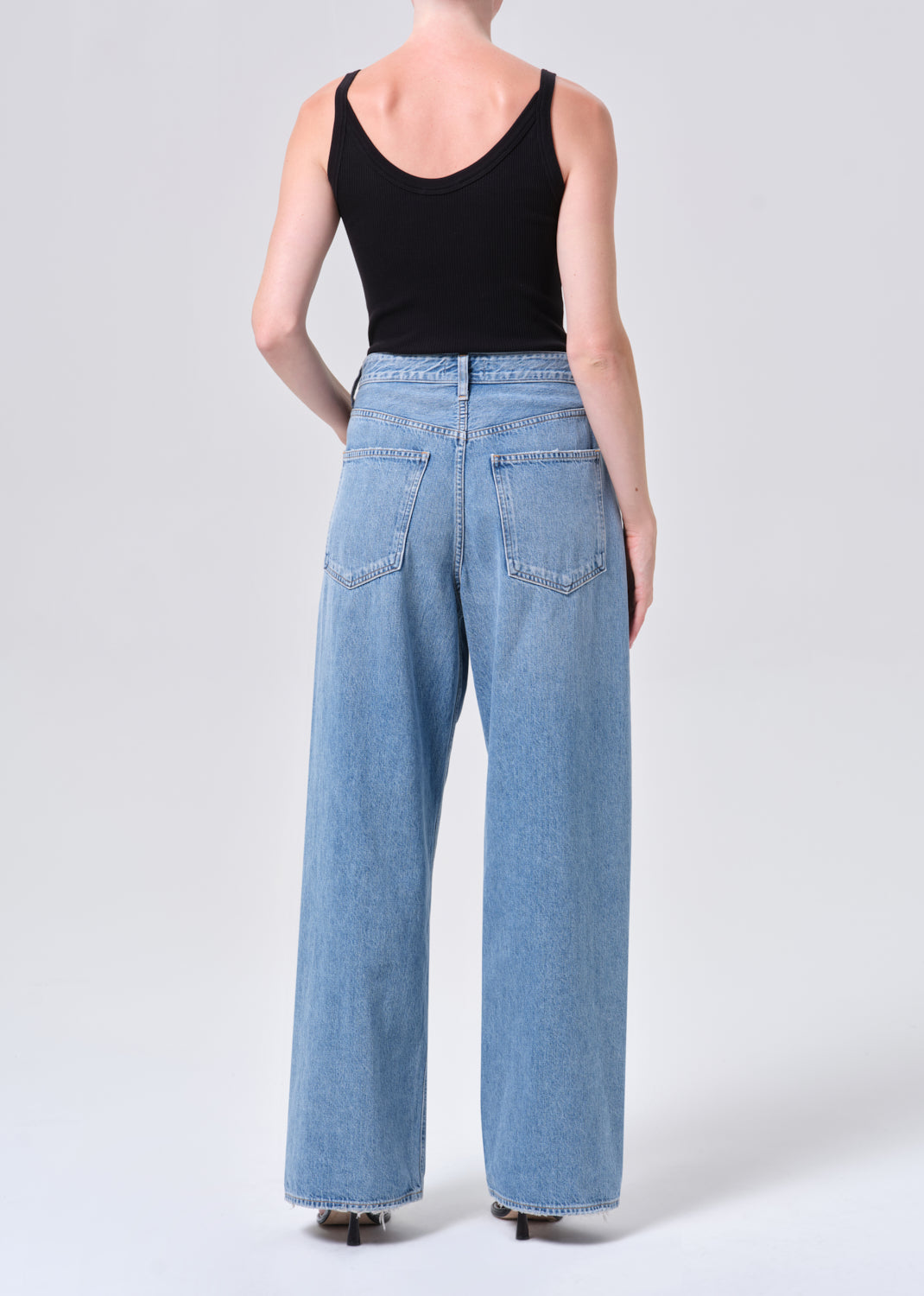 Person wearing light blue jeans and a black tank top on a white background