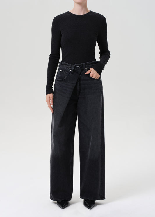 Person wearing a black long-sleeve top and wide-leg black jeans on a white background