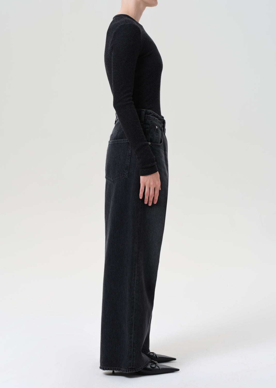 Person wearing black high-waisted pants and a black long-sleeve top on a white background