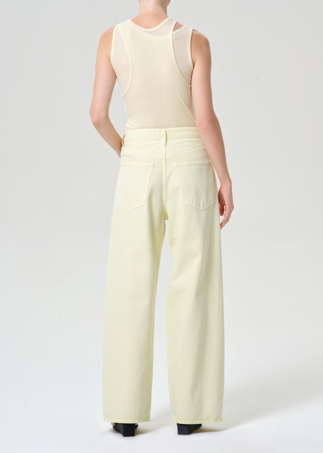 Person wearing a beige sleeveless top and wide-leg pants on a white background