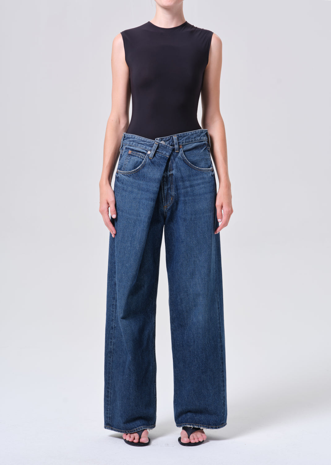 Person wearing a black sleeveless top and blue jeans on a white background