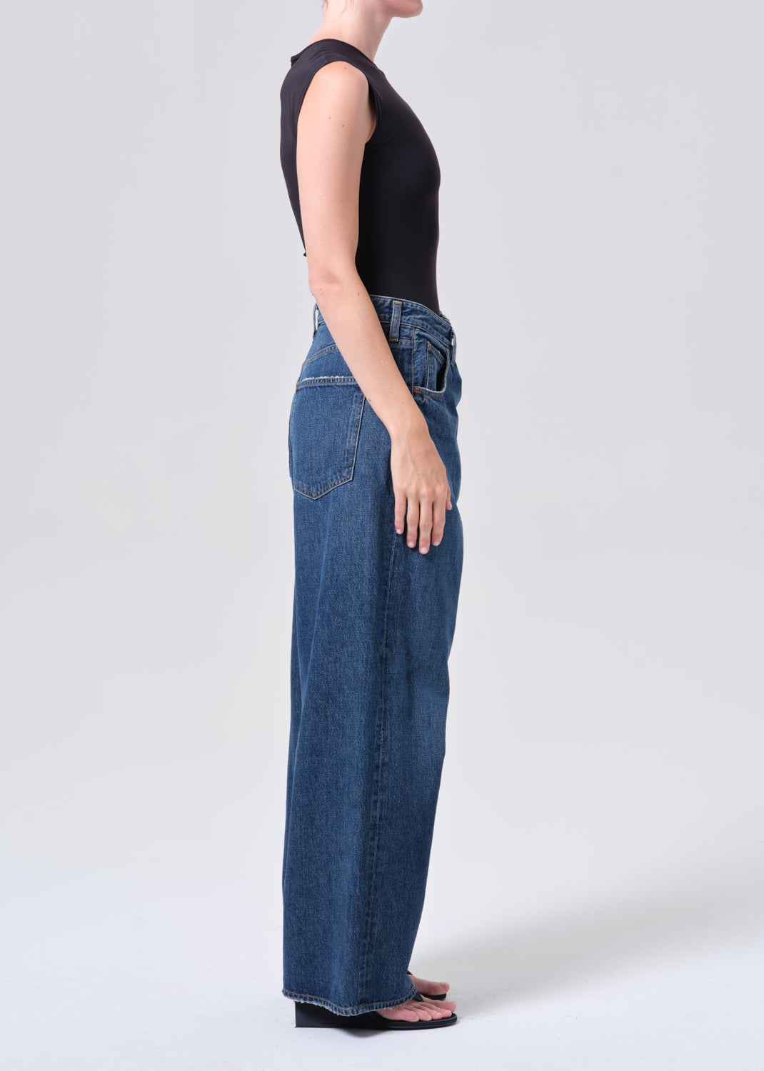 Person wearing blue jeans and a black top on a white background