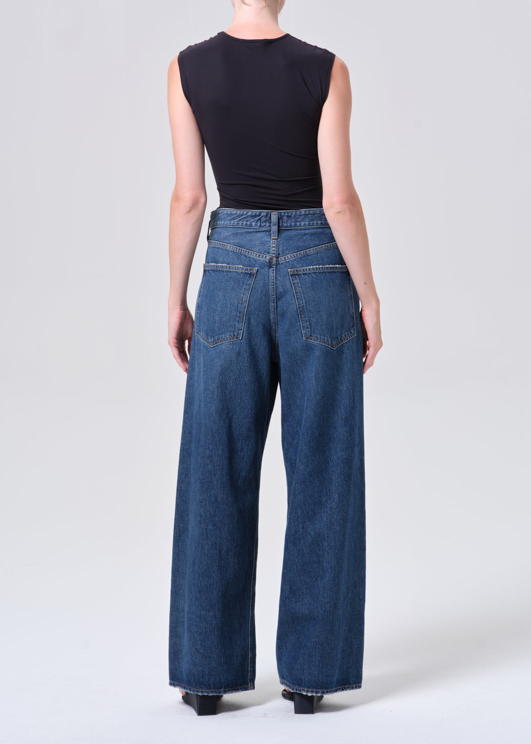 Person wearing blue jeans and a black sleeveless top on a white background