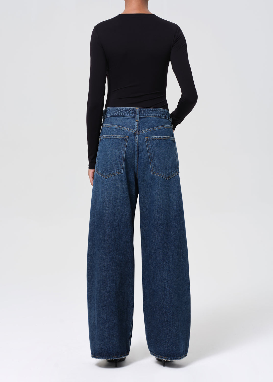 Person wearing blue jeans and a black top on a white background